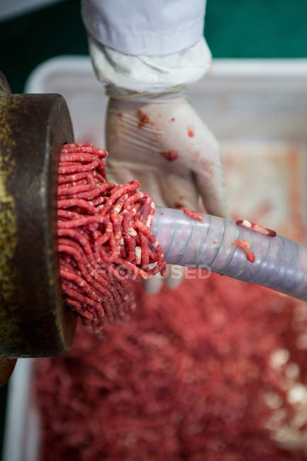 Gros plan sur la viande fraîche hachée dans la machine à hacher et la main du boucher — Photo de stock