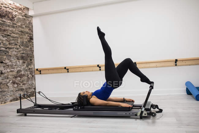 Mujer haciendo ejercicio con los pies en el reformador en el gimnasio - foto de stock