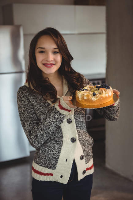 Cheerful woman holding blueberry cake in living room at home — Stock Photo