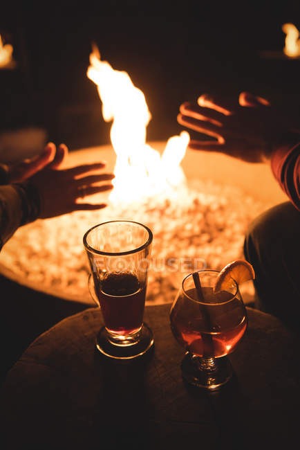Sección media de la pareja sentada junto al fuego y bebidas por la noche durante el invierno - foto de stock