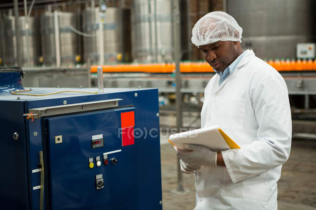 Trabajador serio inspeccionando máquinas en la fábrica de jugo - foto de stock