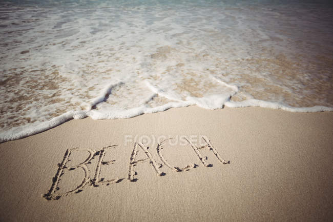 Palavra praia escrita na areia na costa do mar — Fotografia de Stock