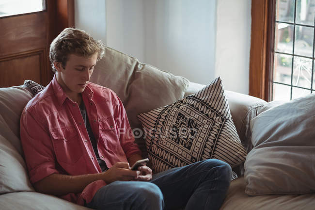 Чоловік сидить на дивані, використовуючи мобільний телефон у вітальні — стокове фото