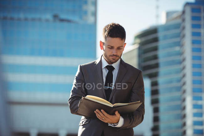 Un homme d'affaires vérifie son journal près d'un immeuble de bureaux — Photo de stock