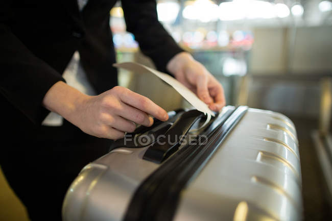 Auxiliar de check-in de la aerolínea pegado al equipaje del viajero en el aeropuerto - foto de stock