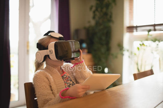 Chica sosteniendo la tableta digital mientras usa auriculares de bienes raíces virtuales en casa - foto de stock