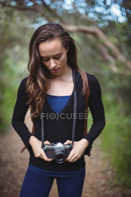 Beautiful woman standing with camera in forest — Stock Photo