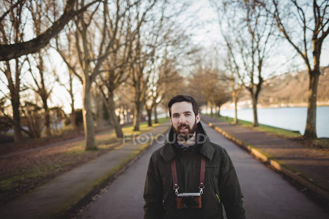 Jeune homme souriant debout avec caméra au bord de la rivière — Photo de stock