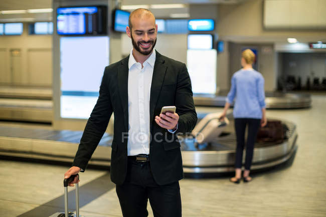 Uomo d'affari in piedi con bagagli utilizzando il telefono cellulare in sala d'attesa presso il terminal dell'aeroporto — Foto stock