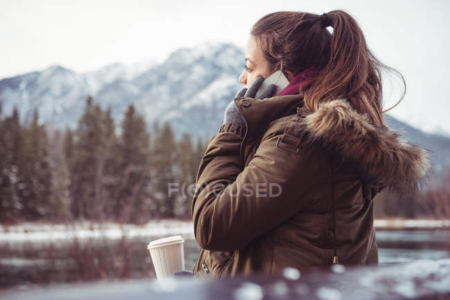 Woman standing on river bank and using mobile phone in winter — Stock Photo