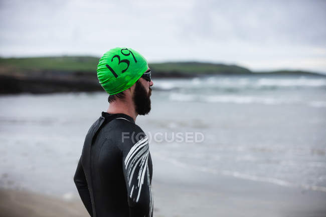 Atleta en traje mojado mirando hacia el mar - foto de stock