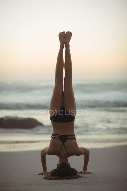 Mulher realizando headstand na praia ao entardecer — Fotografia de Stock