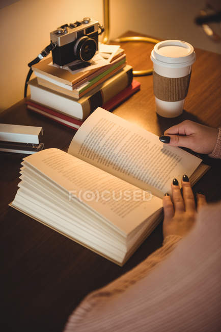 Livre de lecture femme tout en prenant un café dans le salon à la maison — Photo de stock