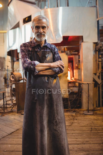 Retrato del soplador de vidrio de pie con los brazos cruzados en la fábrica de soplado de vidrio - foto de stock