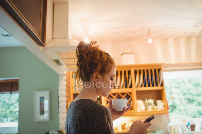 Bella donna che utilizza il telefono cellulare in cucina a casa — Foto stock