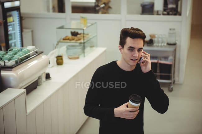 Mann telefoniert mit seinem Handy, während er eine Kaffeetasse in der Hand hält — Stockfoto
