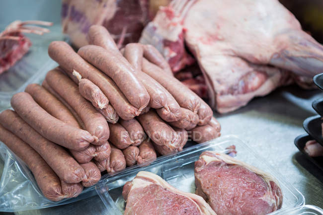 Primer plano de embutidos crudos y carne en bandeja de embalaje de plástico en la fábrica de carne - foto de stock