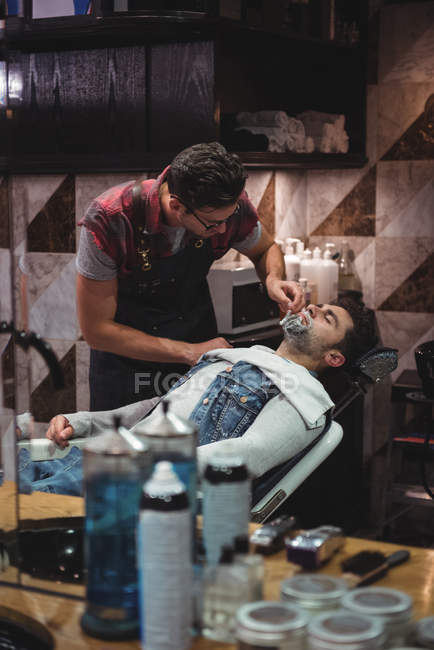 Reflejo del hombre afeitándose la barba por estilista con maquinilla de afeitar en peluquería - foto de stock