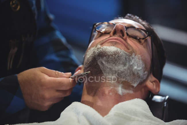 Man getting beard shaved with razor in barber shop — Stock Photo