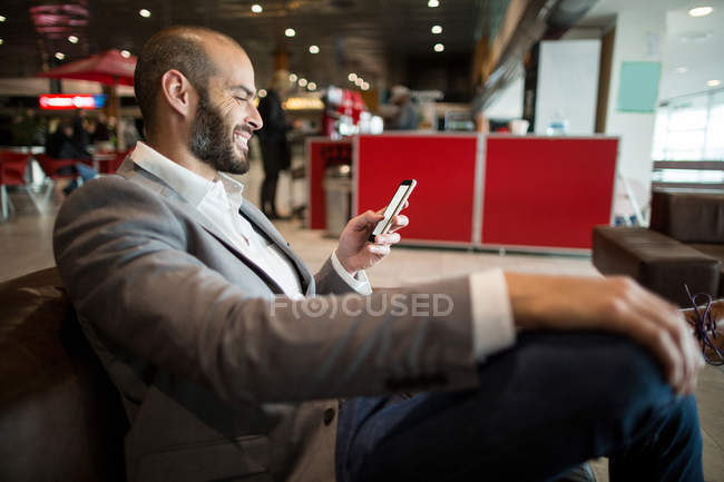 Empresário usando telefone celular na área de espera no terminal do aeroporto — Fotografia de Stock