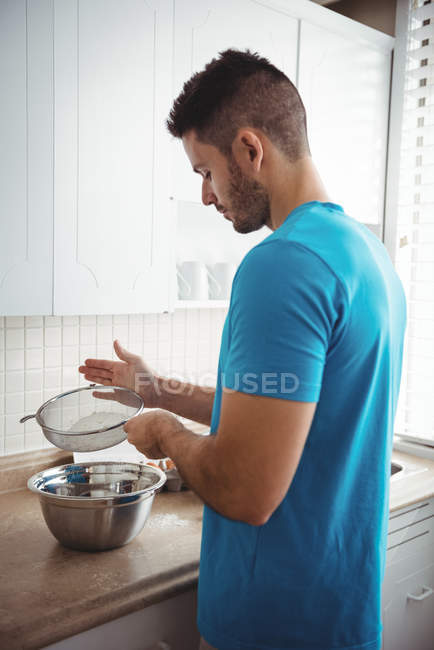 Человек просеивает муку в миску для смешивания на кухне дома — стоковое фото