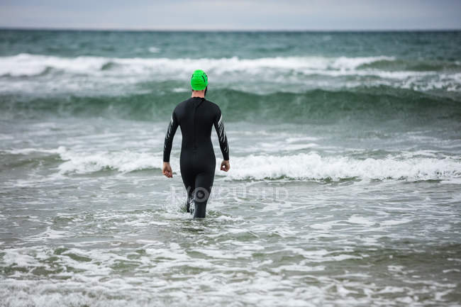 Vista posteriore dell'atleta in muta bagnata che cammina verso il mare — Foto stock