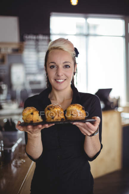 Portrait of waitress holding tray of muffins at counter in cafe — Stock Photo