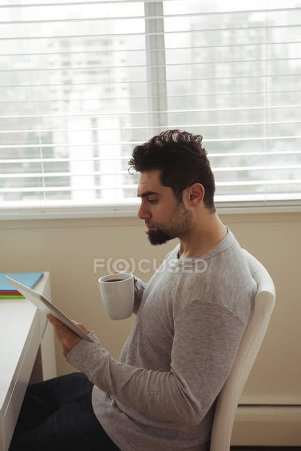 Homme utilisant une tablette numérique tout en prenant un café à la maison — Photo de stock
