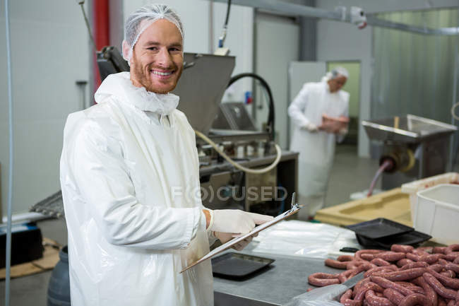 Retrato del carnicero masculino manteniendo registros en el portapapeles en la fábrica de carne - foto de stock
