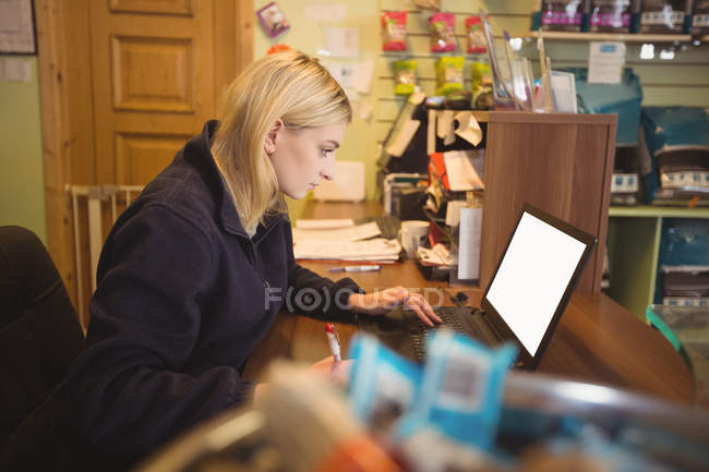 Woman using laptop and writing on notepad in office — Stock Photo