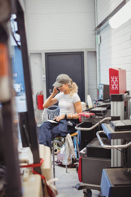 Жінка-механік використовує цифровий планшет під час розмови на мобільному телефоні в ремонті гаража — стокове фото