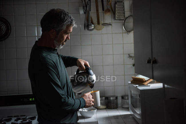 Mann poriert heißes Wasser aus Kolben in Küche — Stockfoto