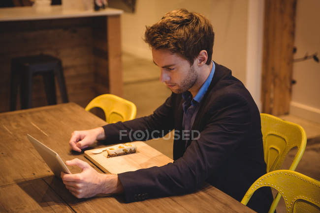Empresário usando tablet digital enquanto faz lanche no café — Fotografia de Stock