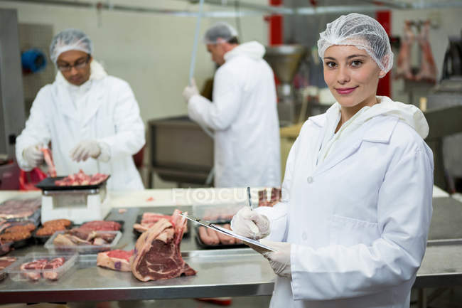 Retrato de la carnicera manteniendo registros en el portapapeles de la fábrica de carne - foto de stock