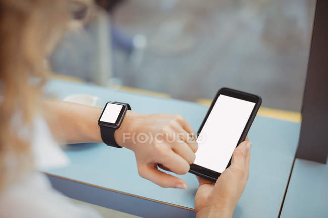 Mãos de mulher de negócios usando móvel e tempo de verificação no balcão na cafetaria — Fotografia de Stock