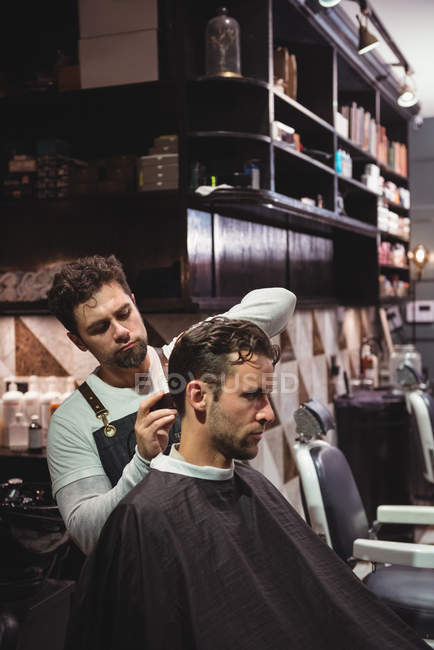 Male barber cutting client hair with trimmer in barbershop — Stock Photo
