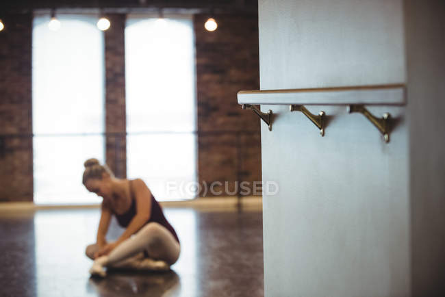 Soporte de barra de ballet en estudio de ballet con mujer atando cordones en el fondo - foto de stock