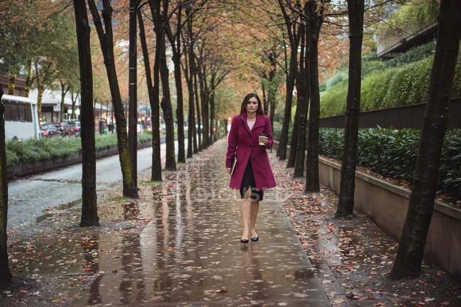 Femme d'affaires avec journal marche sur passerelle piétonne humide pendant la journée — Photo de stock
