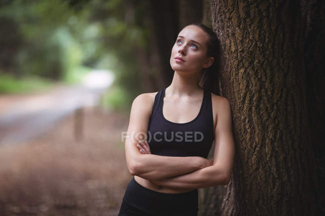 Задумчивая женщина, опирающаяся на дерево в лесу — стоковое фото