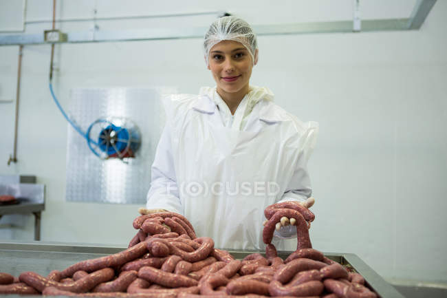 Retrato de açougueiro fêmea segurando salsichas na fábrica de carne — Fotografia de Stock