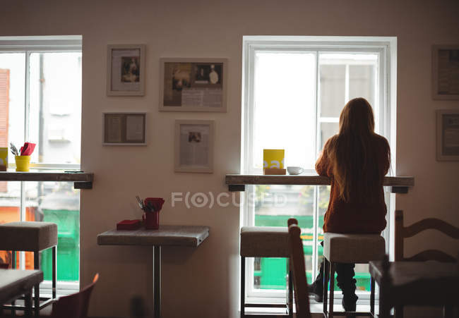 Vue arrière de la femme assise à la fenêtre dans l'intérieur du restaurant — Photo de stock