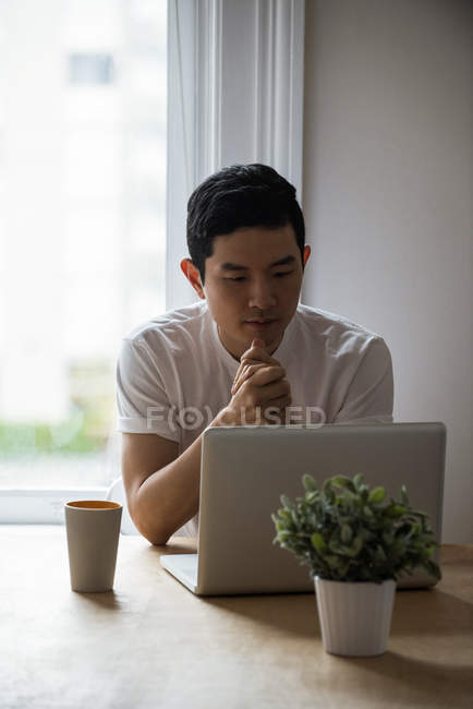 Homem olhando para laptop com uma xícara de café na mesa em casa — Fotografia de Stock
