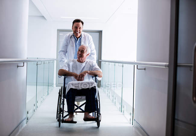 Врач взаимодействует с пожилым мужчиной на инвалидной коляске в коридоре — стоковое фото