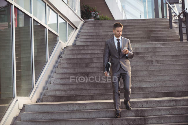 Uomo d'affari che utilizza il telefono cellulare mentre cammina lungo i gradini — Foto stock