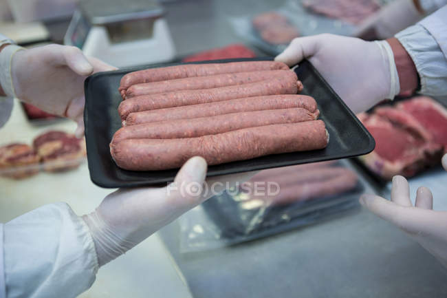 Macellai che imballano salsicce crude in vassoio di imballaggio di plastica in fabbrica di carne — Foto stock