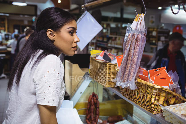 Pensativo personal femenino de pie en el mostrador de carne en el supermercado - foto de stock