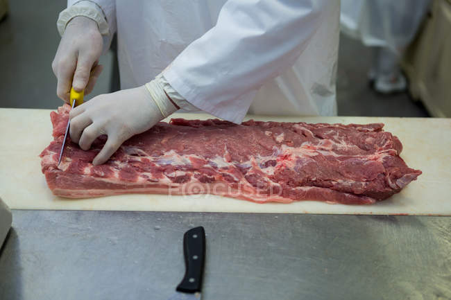 Mid section of butcher cutting meat at meat factory — Stock Photo
