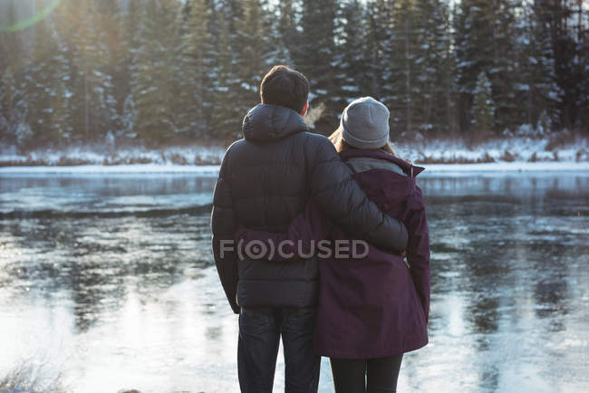 Задний вид романтической пары, стоящей у реки зимой — стоковое фото