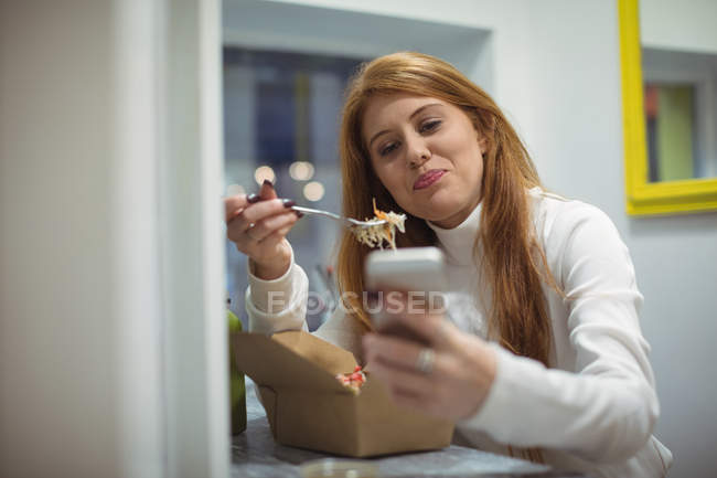 Mujer joven usando el teléfono móvil mientras come ensalada en la cafetería - foto de stock