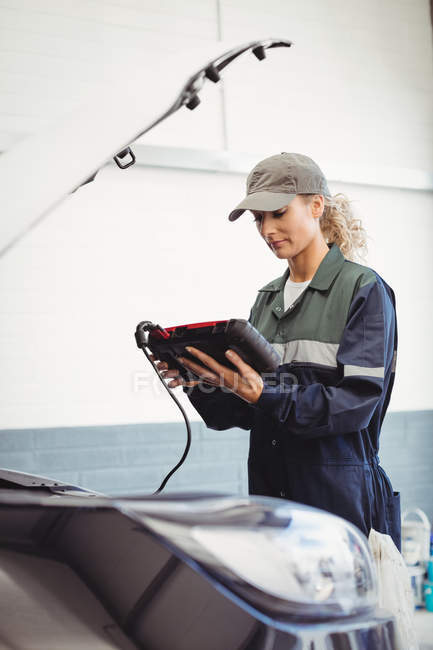 Mécanicien féminin utilisant un dispositif de diagnostic électronique dans le garage de réparation — Photo de stock